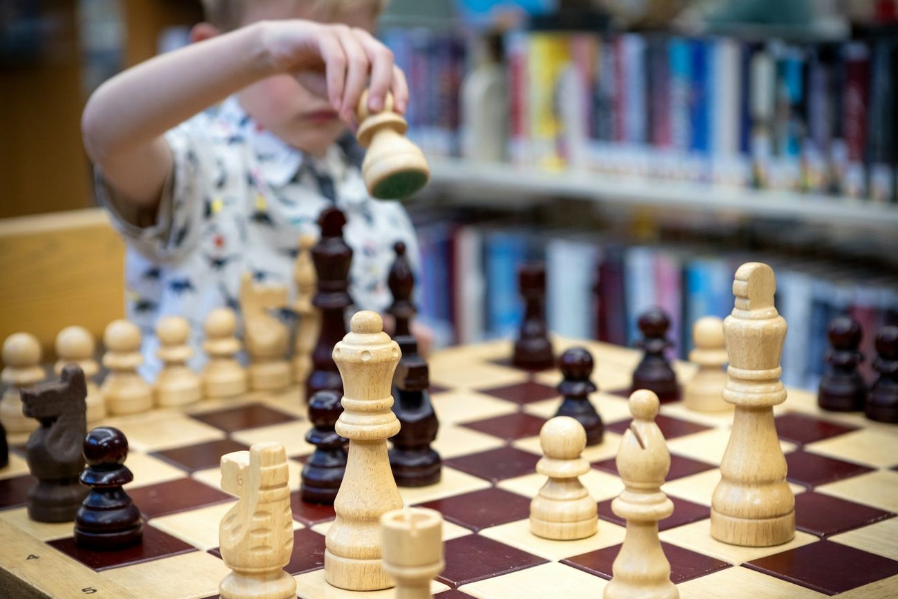 A young student moving a piece on a chessboard in a library