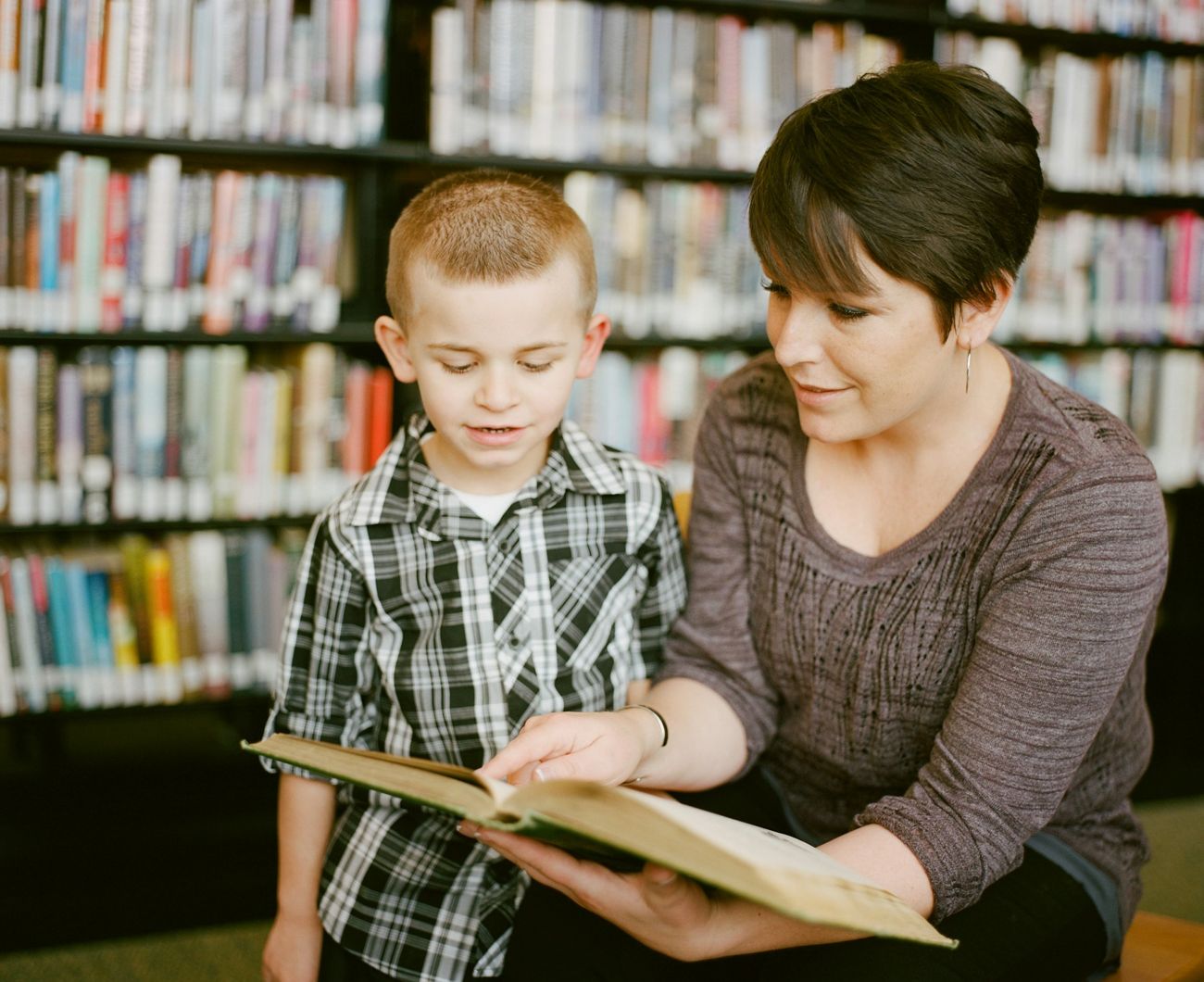 Une tutrice lit un livre avec un jeune garçon dans une bibliothèque